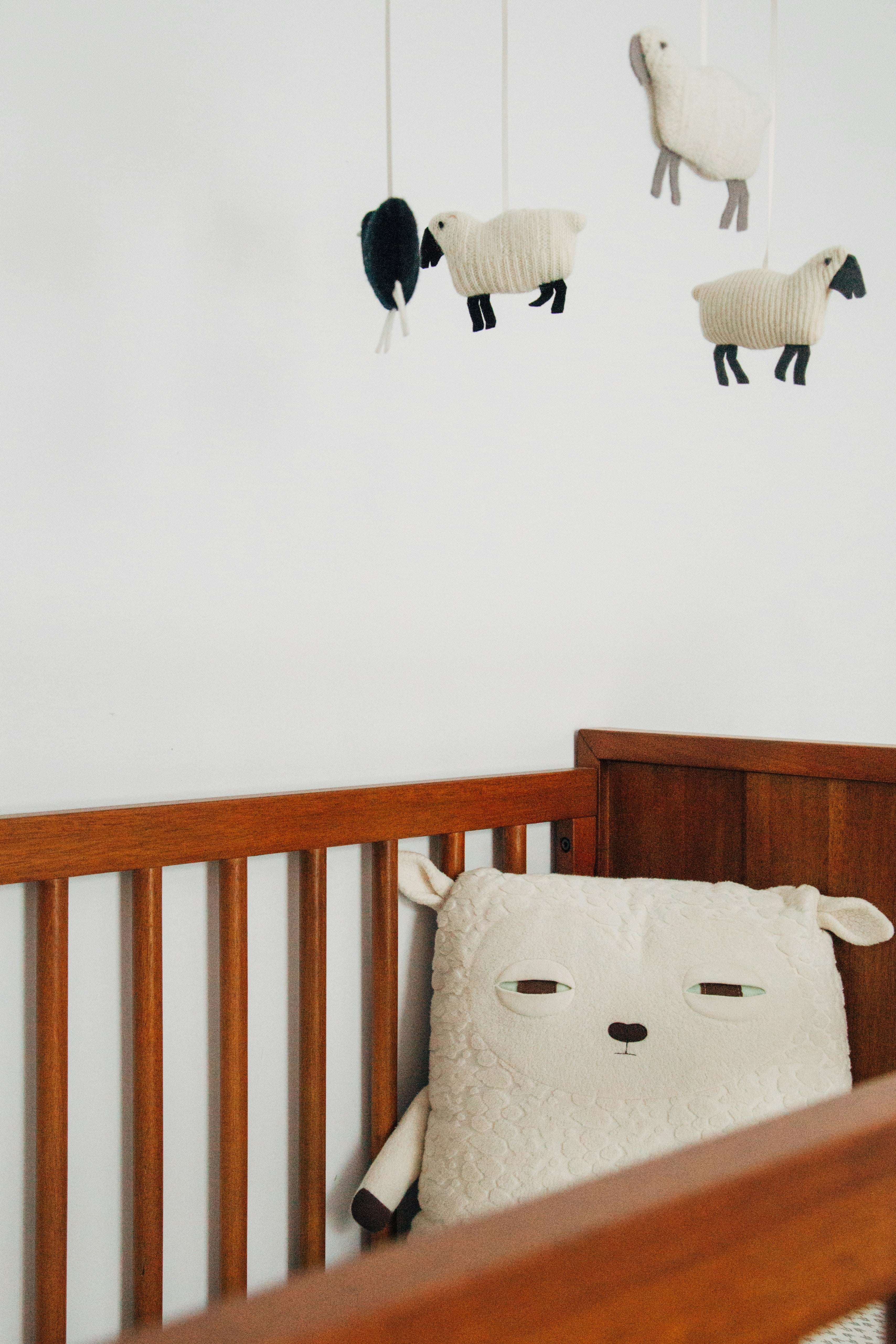 Wooden crib with sheep-themed mobile and pillow against a white wall