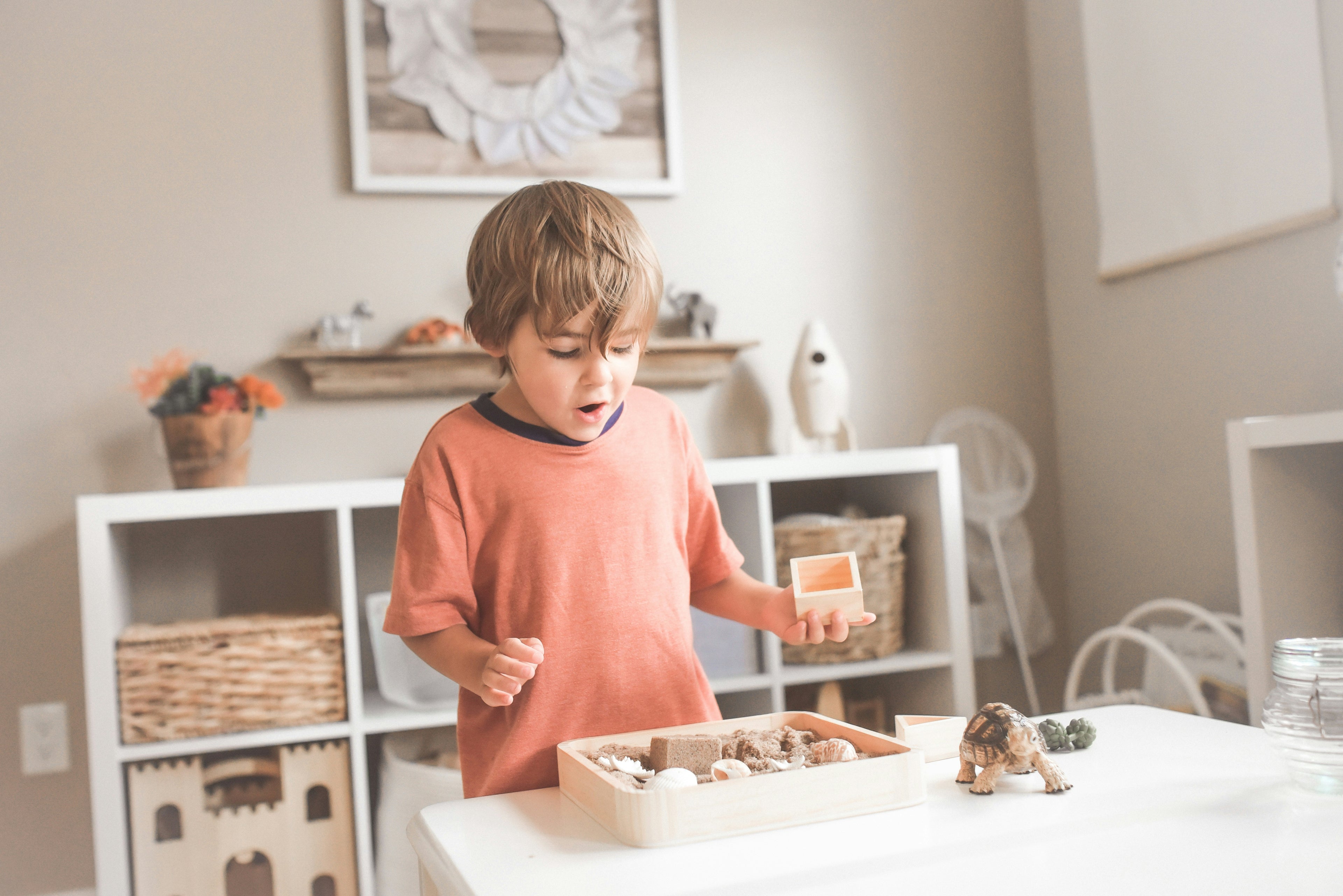 Child playing with toys on a table in a room with shelves and decor.