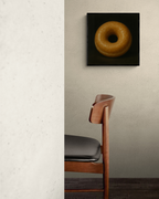 Framed print of a glazed donut above a wooden chair.