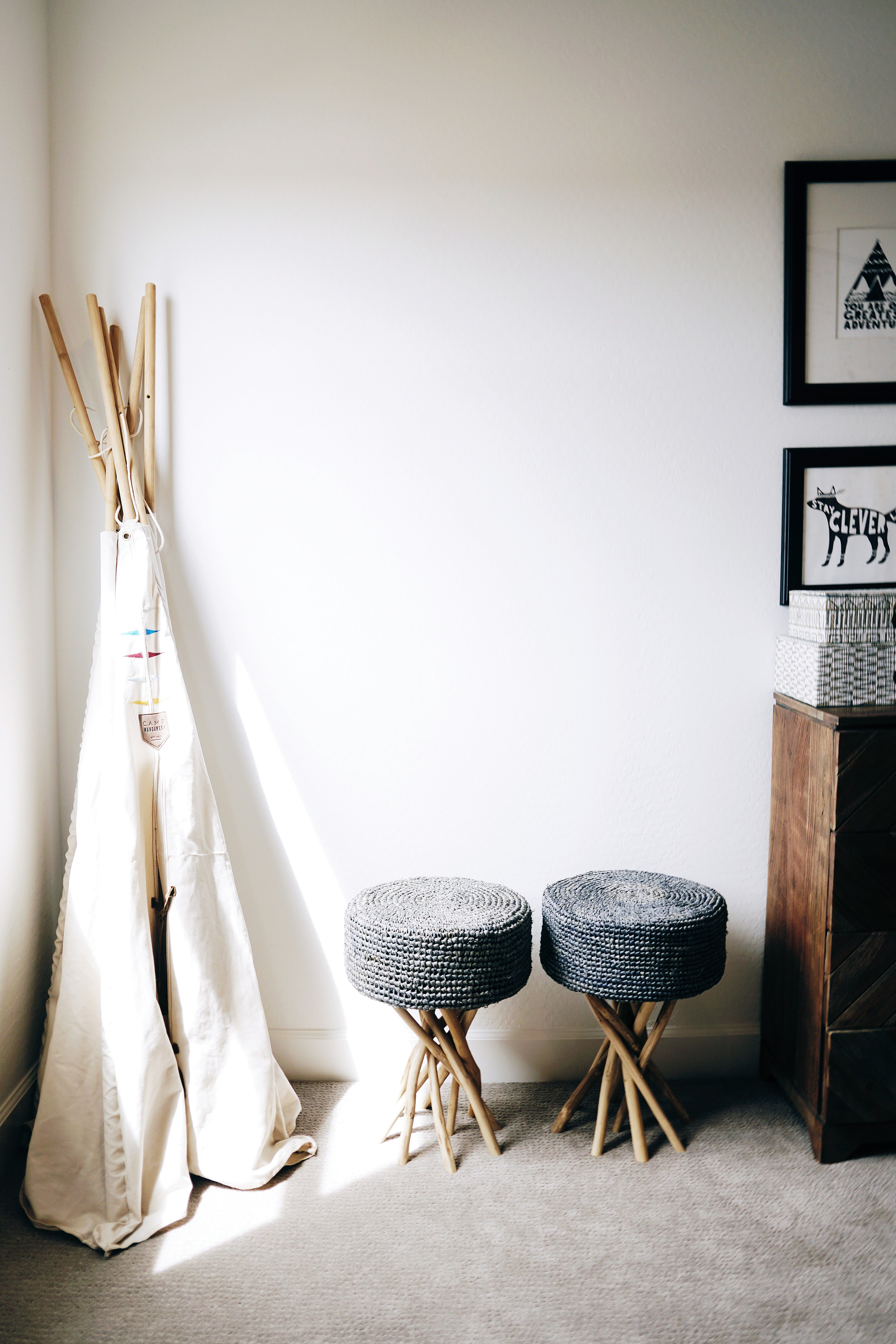 Children's playroom with a teepee, stools, and framed pictures on a white wall.