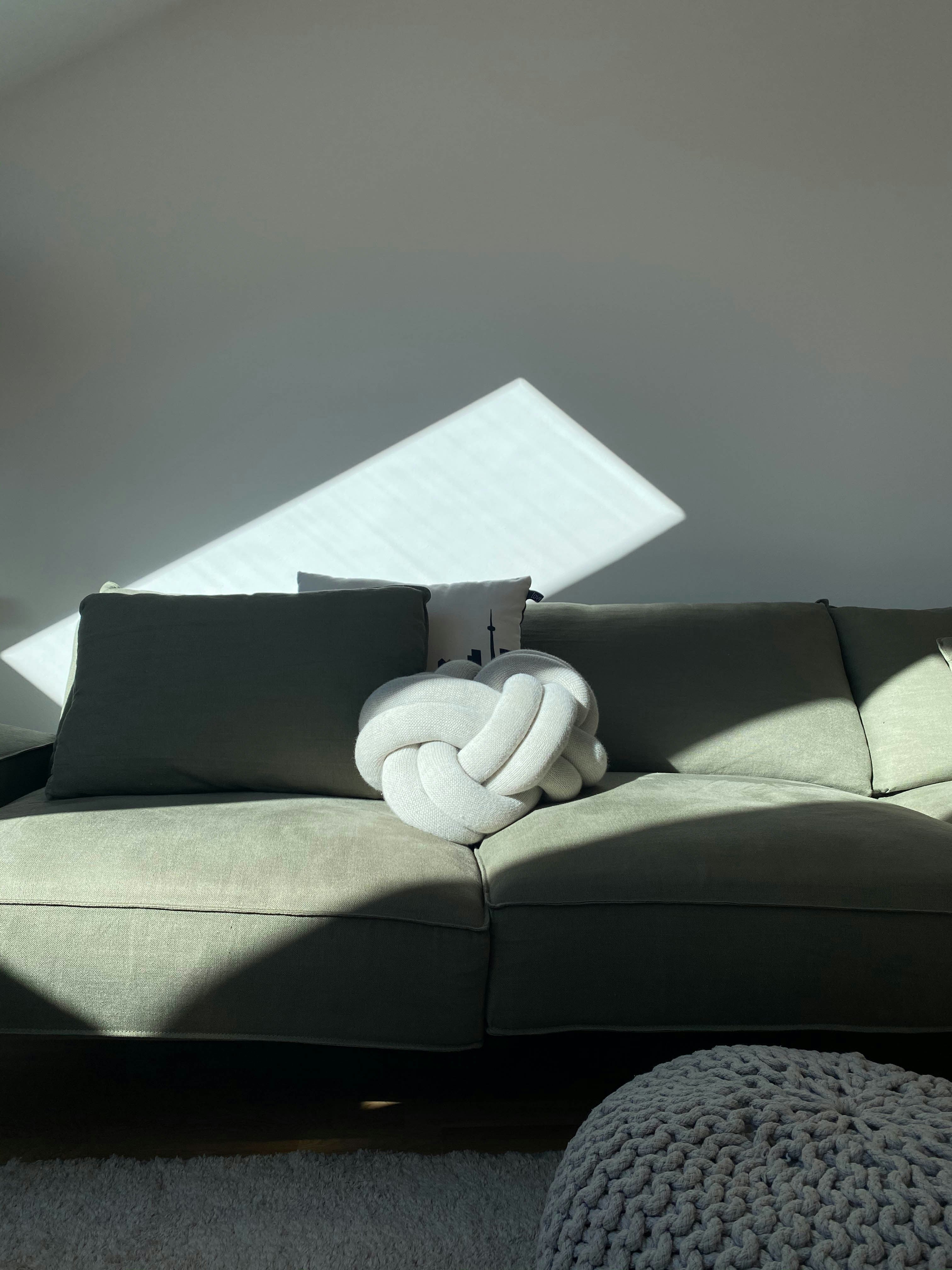 Gray sofa with decorative pillows in a room with sunlight casting shadows.